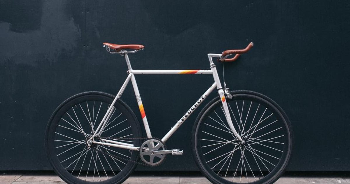 A white road bike with an orange saddle against a dark wall