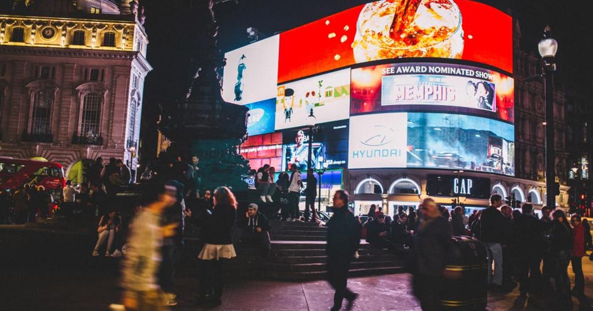 Bright advertising screens over a busy city square at night